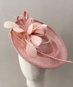 Tocado en tono rosa de sinamay para invitada con raquis y plumas. Se coloca con diadema y es cómodo y elegante.