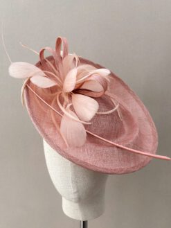 Tocado en tono rosa de sinamay para invitada con raquis y plumas. Se coloca con diadema y es cómodo y elegante.