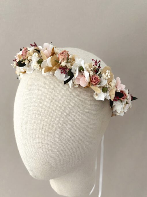Corona de flores preservadas en tonos blancos y rosas suaves. Perfecta para cualquier estilo de vestido de Primera Comunión. Está terminada con una lazada para ajustarla a la medida que resulte más cómoda.